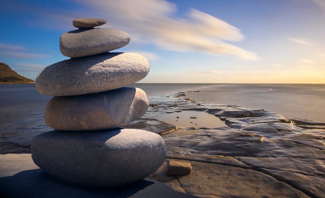 about-me-01 A serene stack of stones on the rocky seashore during a peaceful sunrise, embodying balance and zen.