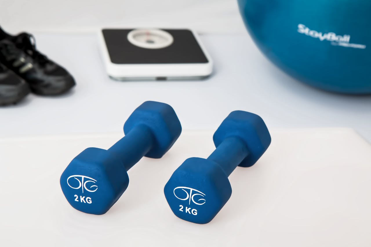 hero-img Blue dumbbells placed on a white surface with fitness equipment in the background.